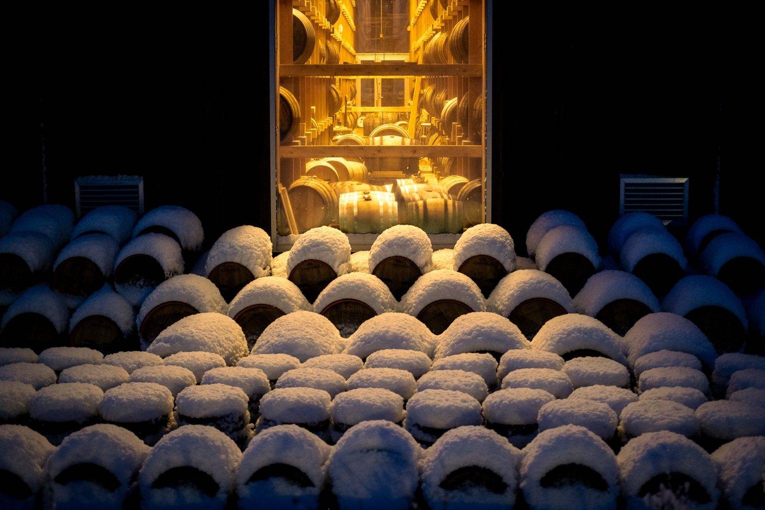 Fûts enneigés devant un chai éclairé de la distillerie Myken la nuit