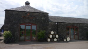 Façade extérieure de la distillerie Strathearn, petite distillerie artisanale du Perthshire, avec quelques fûts alignés devant le bâtiment.