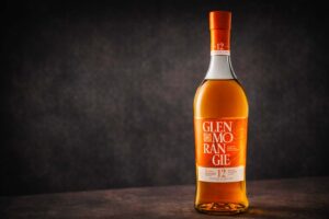 Bouteille de Glenmorangie The Original 12 ans photographiée seule sur une surface sombre, avec un fond neutre texturé et une lumière douce.