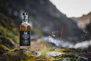 Bouteille de Flóki Icelandic Single Malt Whisky posée sur un sol moussu dans un paysage islandais rocheux