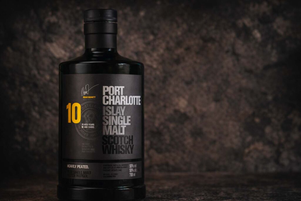 Bouteille de Port Charlotte 10 photographiée seule sur une surface sombre, avec un fond minéral texturé et une lumière douce.